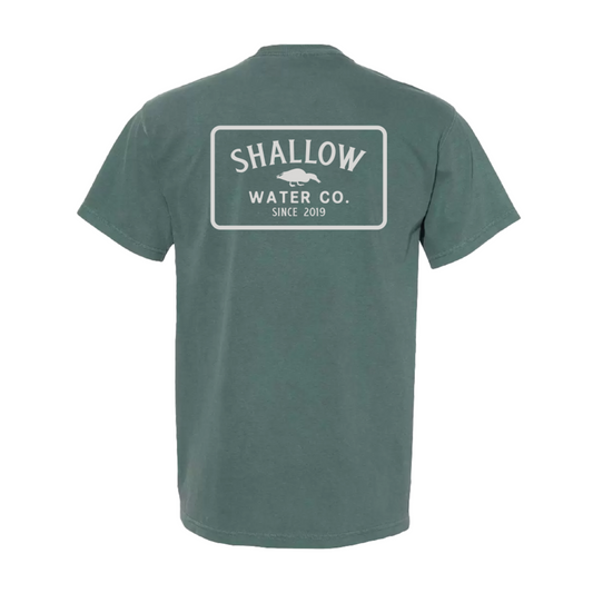 Flat lay of Blue Spruce Icon Tee featuring large Shallow Water Co. logo on the back, set against a neutral background.
